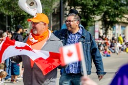 Canada flags flap in front of Naheed Nenshi and supporters marching in the parade while they greet parade watchers in Red Deer.